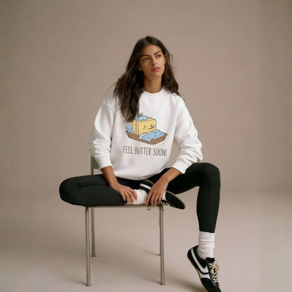 Woman wearing a white sweatshirt with a graphic design sitting on a chair against a beige background