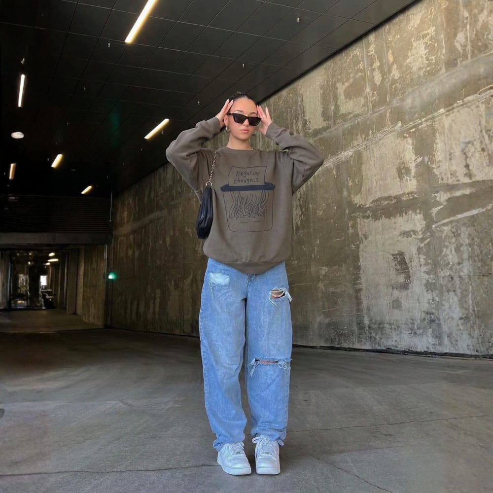 Person wearing a gray sweatshirt and light blue jeans standing in an industrial setting.