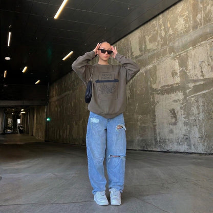 Person wearing a gray sweatshirt and light blue jeans standing in an industrial setting.