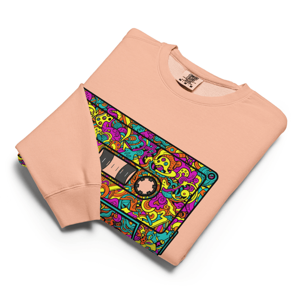 Folded peach sweatshirt with a colorful cassette tape design on a white background