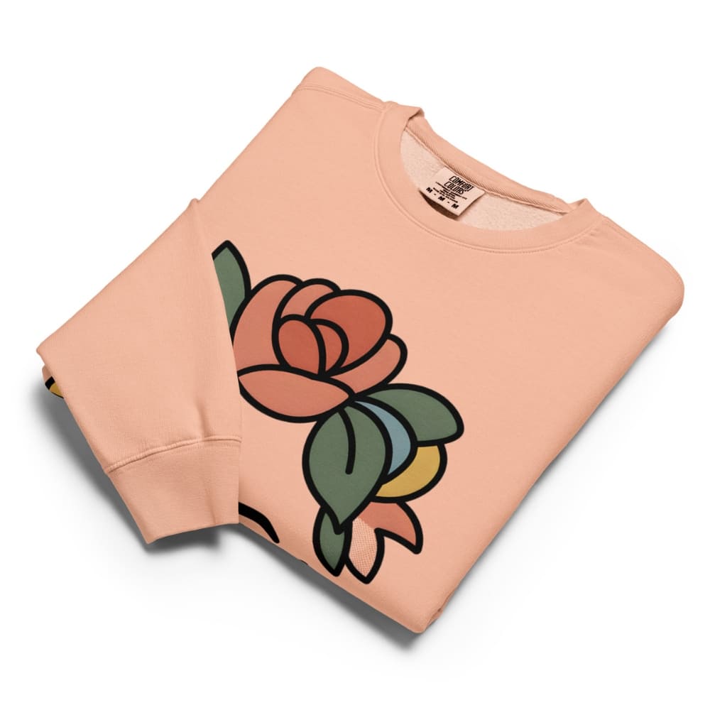 Folded peach-colored sweatshirt with a large rose graphic on a white background