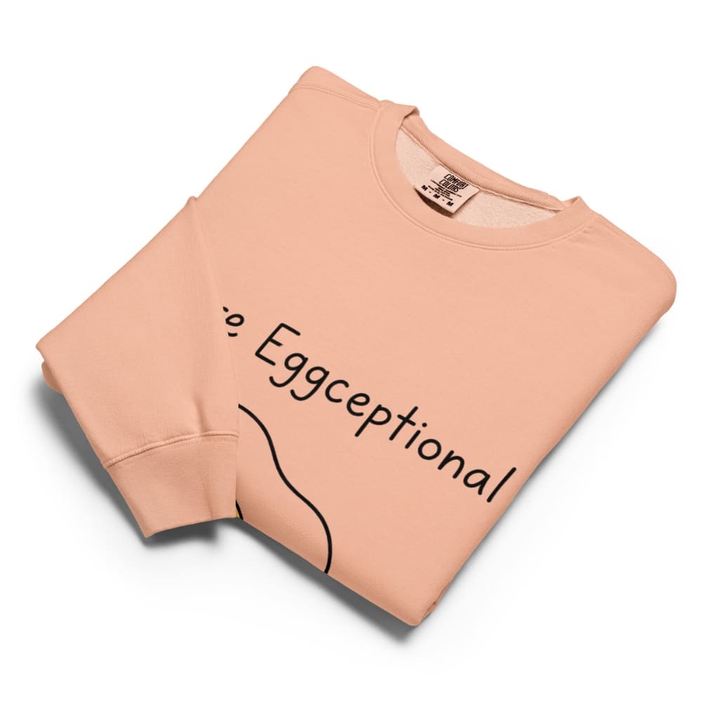 Folded peach-colored sweatshirt with 'Eggceptional' text on a white background