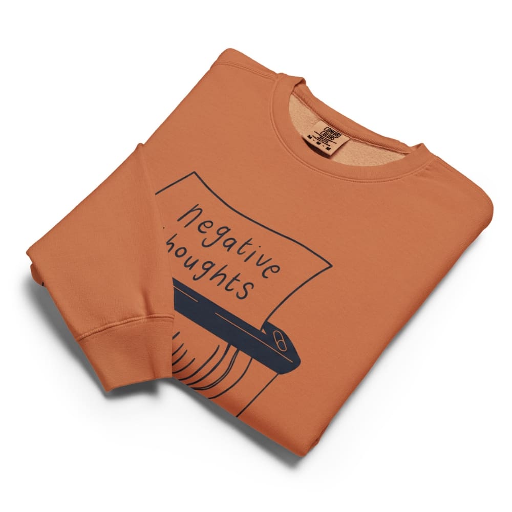 Folded orange sweatshirt with 'negative thoughts' graphic on a white background