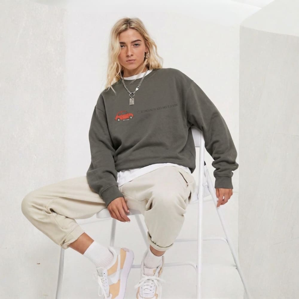 Person wearing a gray sweatshirt with a red graphic, beige pants, and white sneakers on a white background