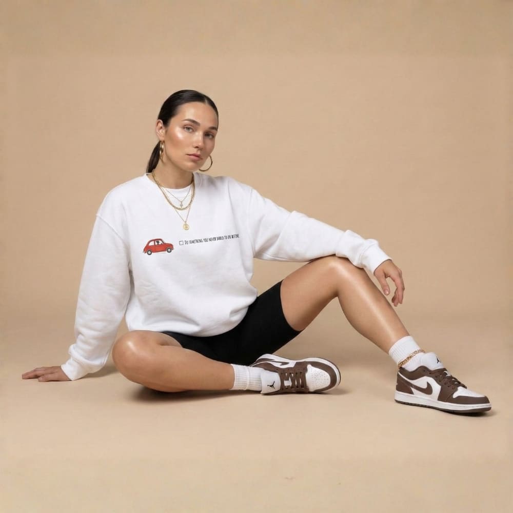 Woman wearing a white sweatshirt with a red car design, sitting on a beige background