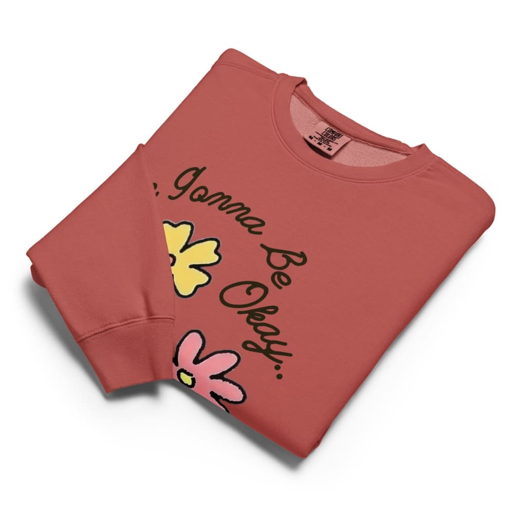Folded red sweatshirt with 'It's Gonna Be Okay' text and flower graphics on a white background