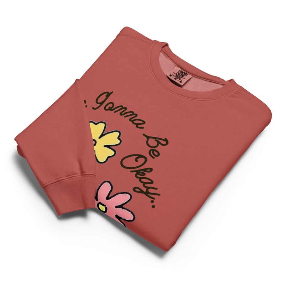 Folded red sweatshirt with 'It's Gonna Be Okay' text and flower graphics on a white background