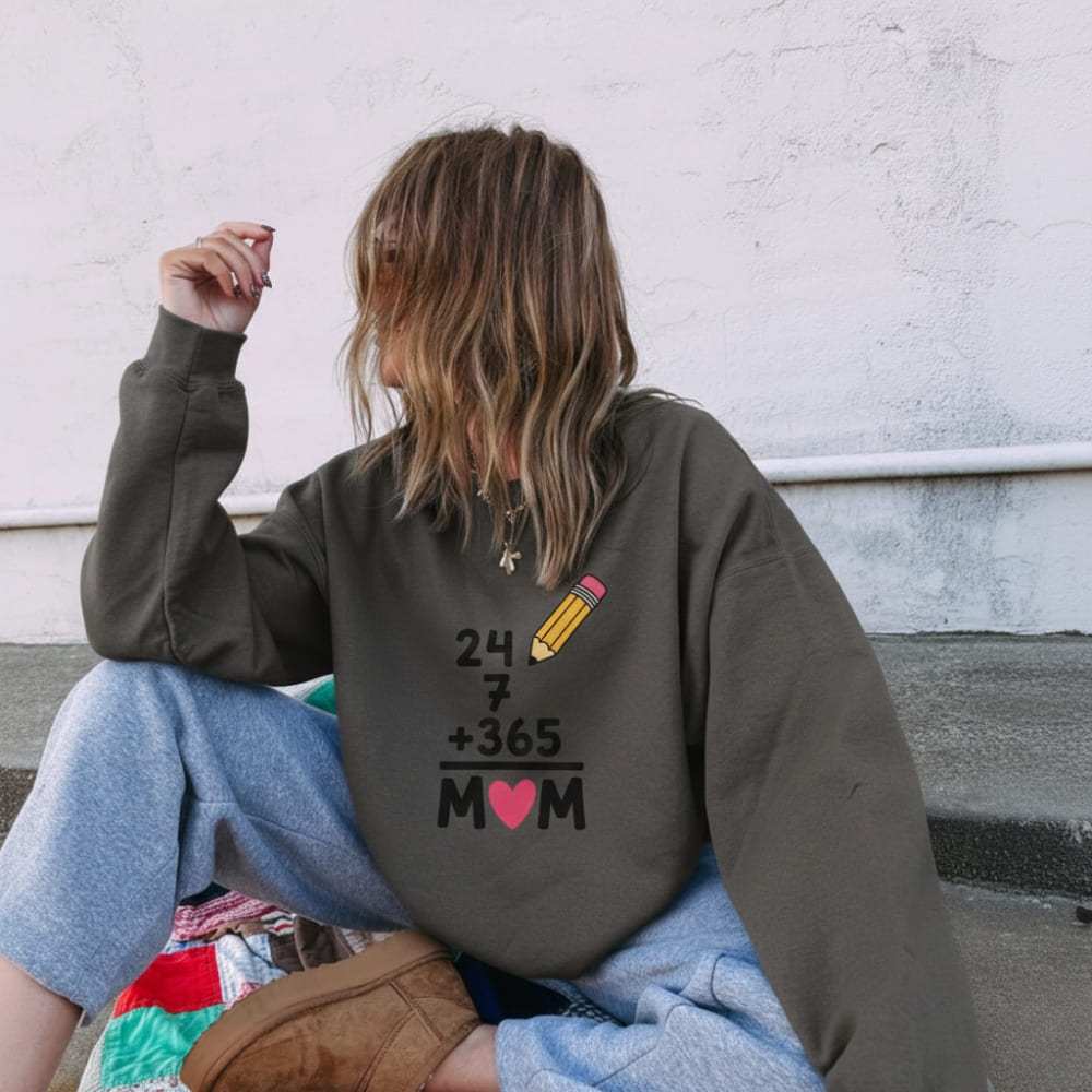 Person wearing a sweatshirt with a unique design on the back, sitting against a white wall.