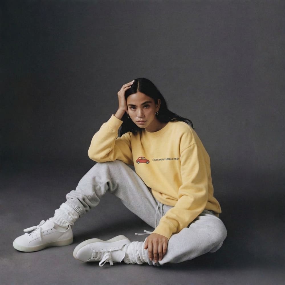 Person wearing a yellow sweatshirt and gray pants sitting on a dark background