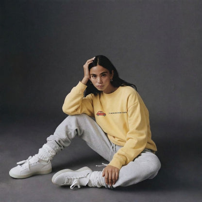 Person wearing a yellow sweatshirt and gray pants sitting on a dark background