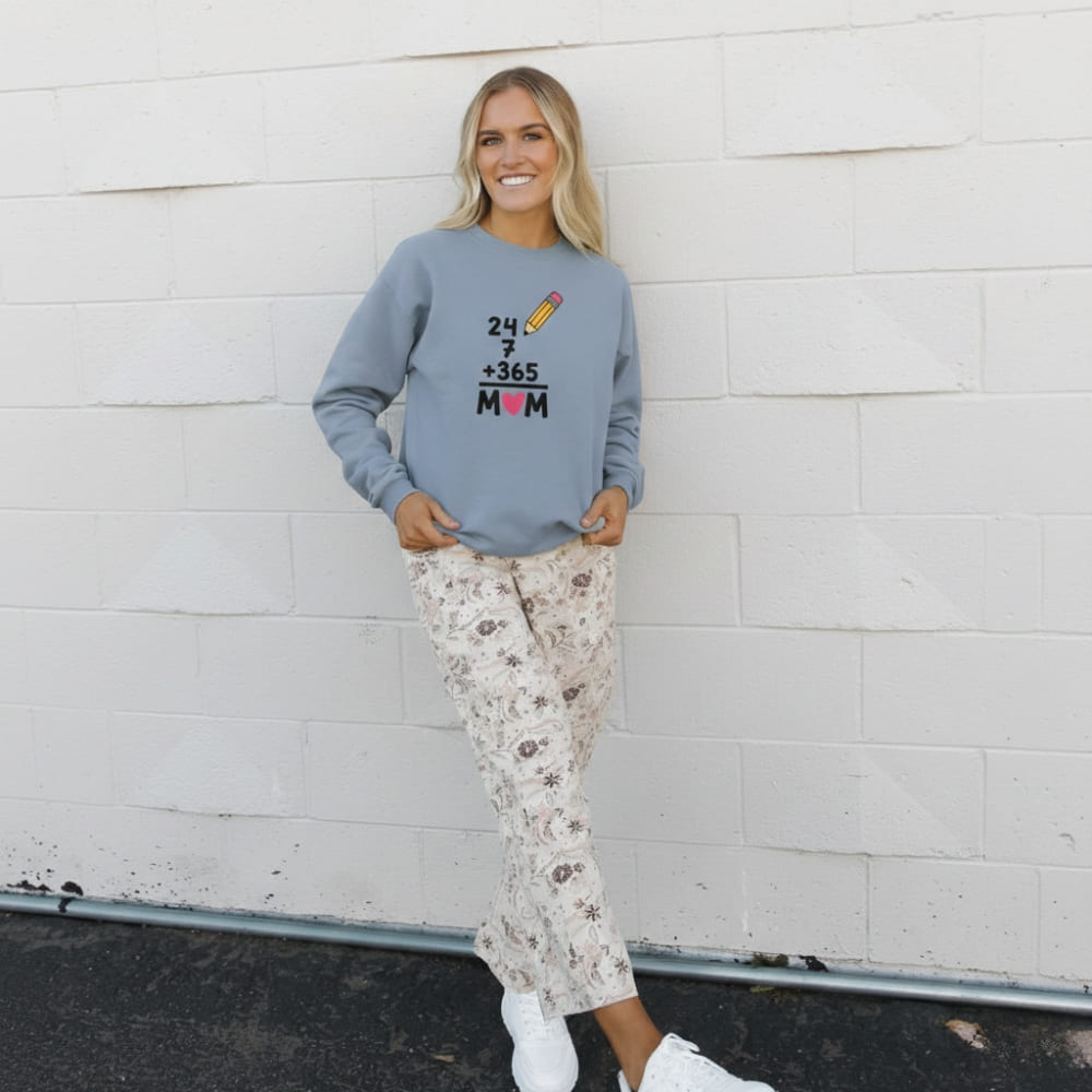 Woman wearing a blue sweatshirt with text and floral pants against a white wall.