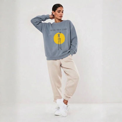 Person wearing a blue sweatshirt with a yellow graphic and text, beige pants, and white sneakers on a light gray background