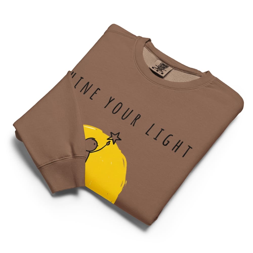 Brown sweatshirt with yellow graphic and 'Shine Your Light' text on a white background