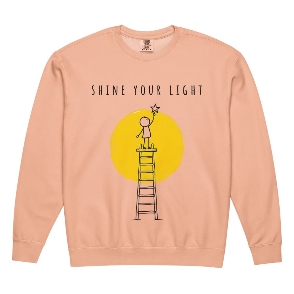 Peach-colored sweatshirt with 'Shine Your Light' graphic and text on a white background