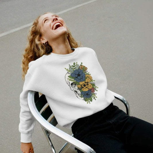 Person wearing a white sweatshirt with a floral and skull design, sitting on a chair against a plain background.