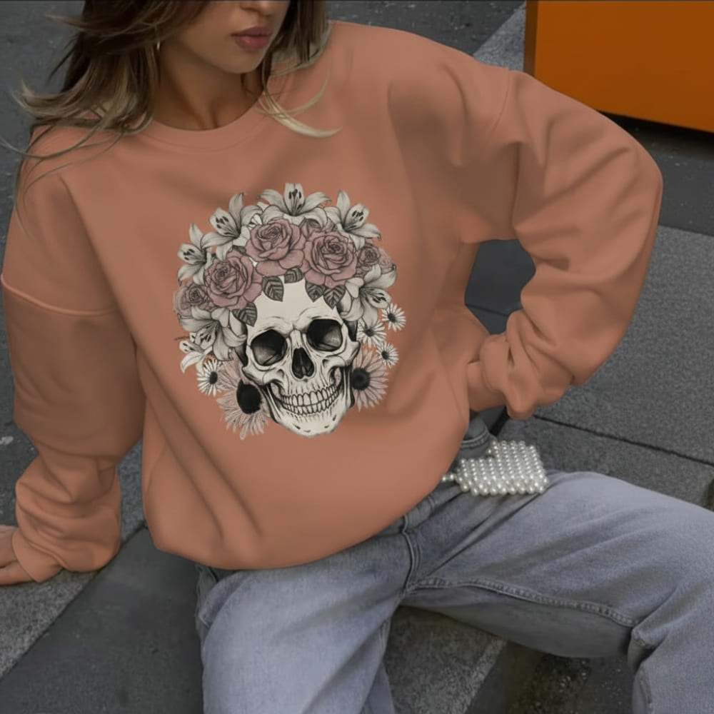 Person wearing a orange sweatshirt with a skull and floral design, sitting on a bench.