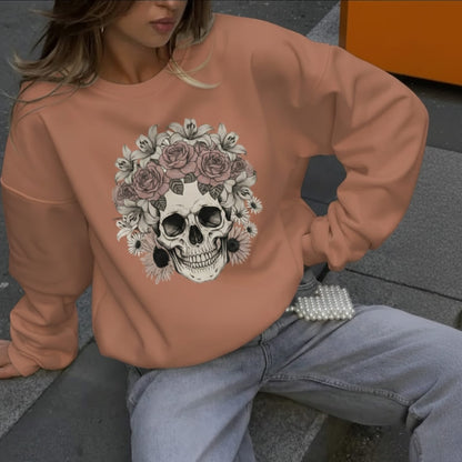 Person wearing a orange sweatshirt with a skull and floral design, sitting on a bench.