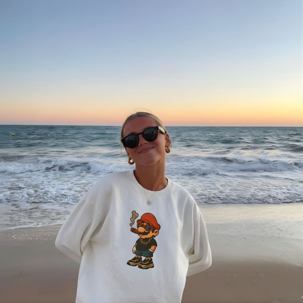 Person wearing a white sweatshirt with a graphic design on a beach at sunset