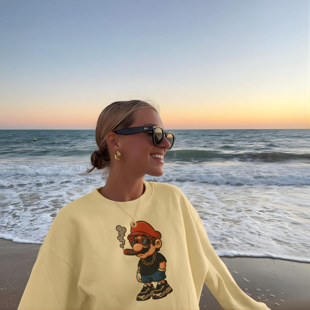 Person wearing a yellow sweatshirt with a graphic design on a beach at sunset