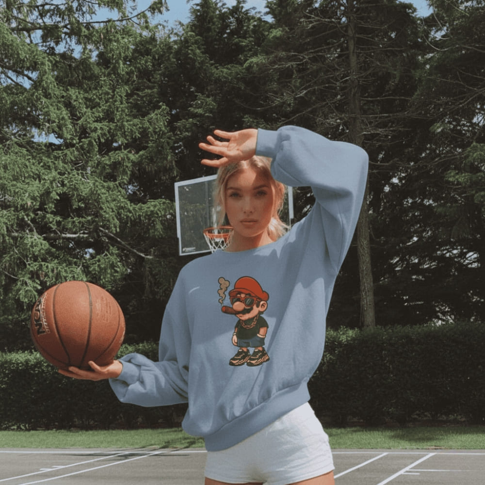 Person wearing a blue sweatshirt with a cartoon character holding a basketball on an outdoor court.