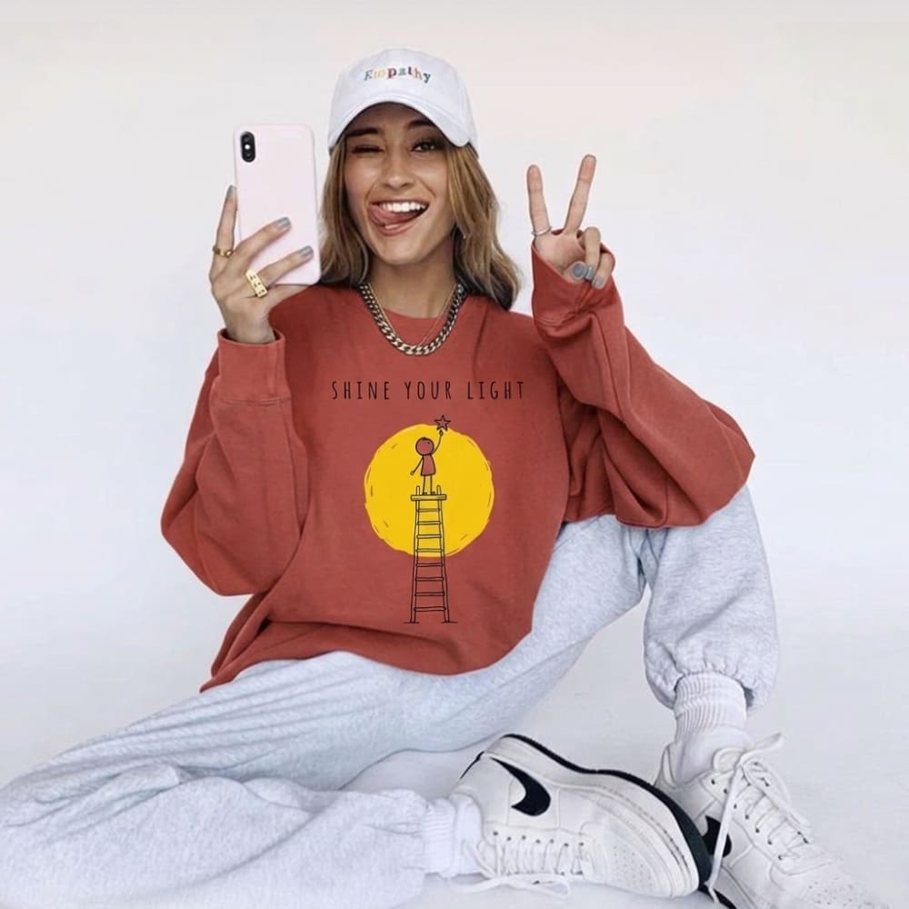 Person wearing a red sweatshirt with a graphic design, white cap, and white pants on a plain background