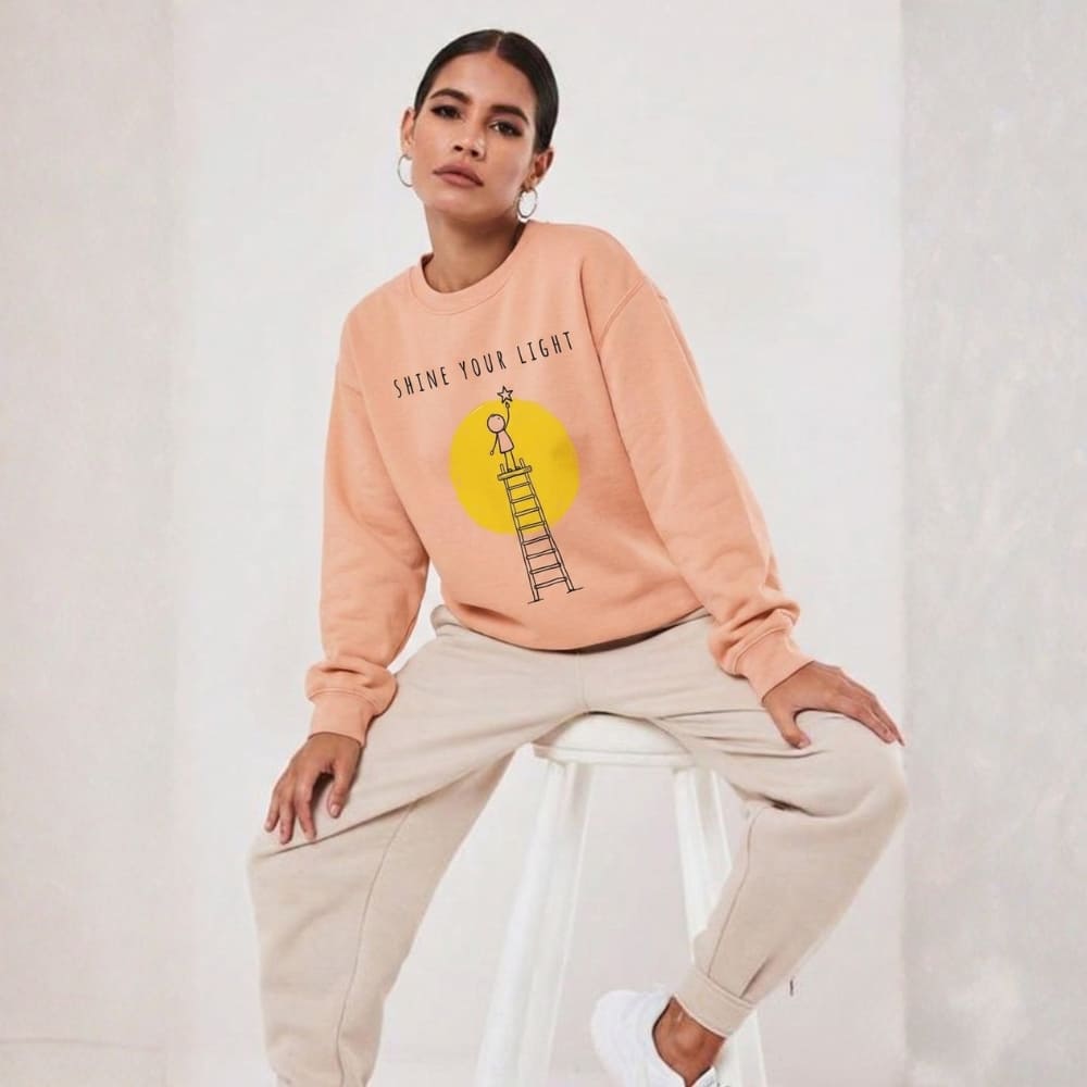 Person wearing a peach-colored sweatshirt with a graphic design on a white background