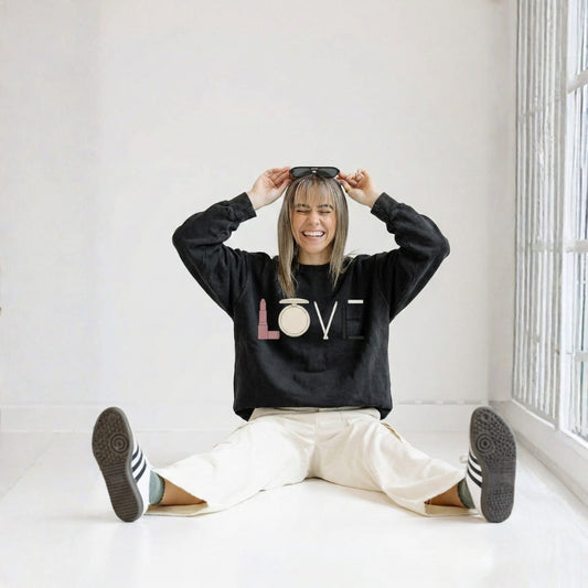 Person wearing a black sweatshirt with 'LOVE' printed on it, sitting on the floor in a bright room.