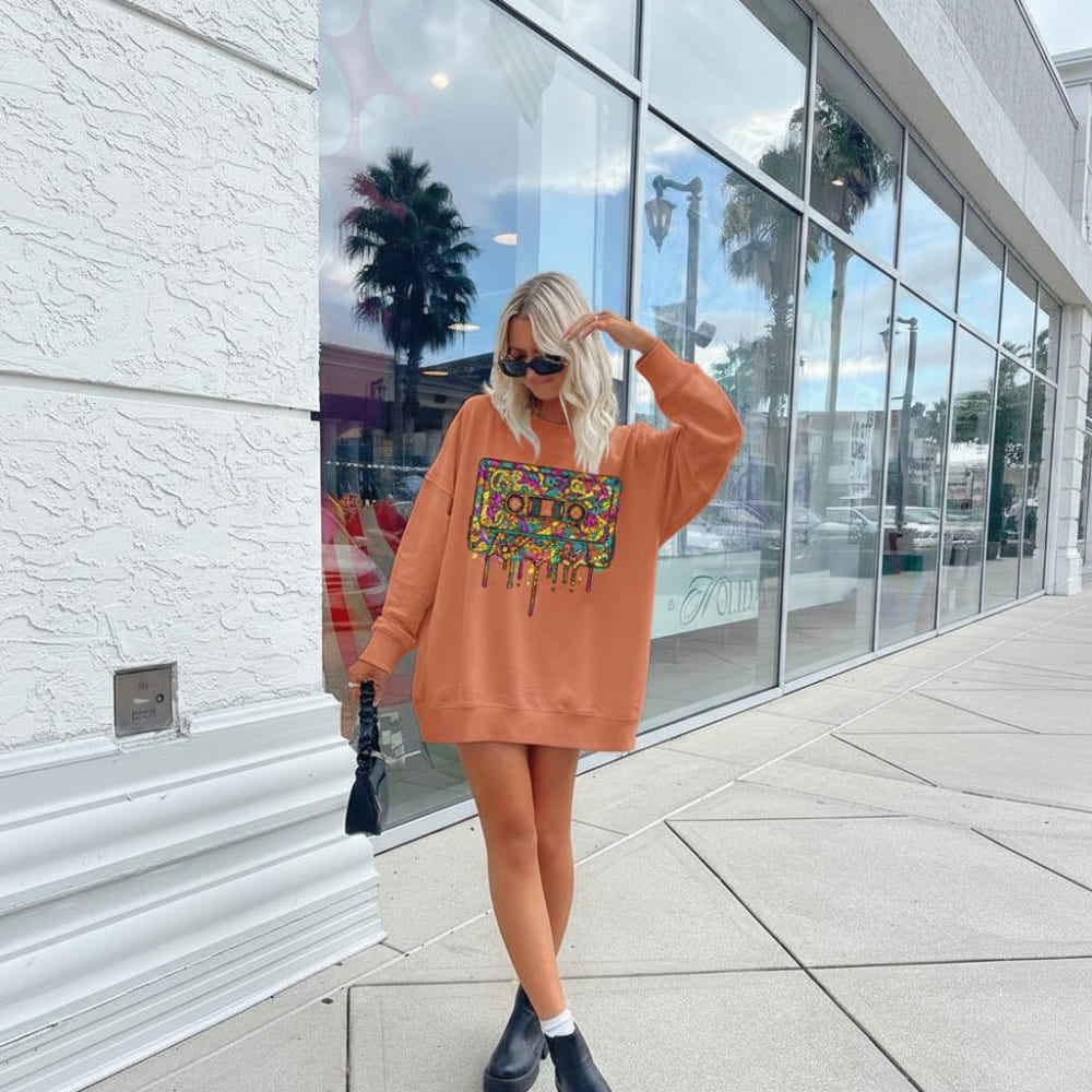 Person wearing a colorful sweatshirt with a graphic design, standing on a sidewalk.