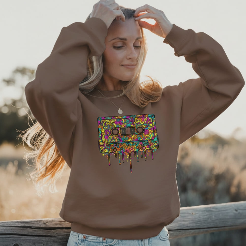 Woman wearing a brown sweatshirt with a colorful cassette tape design outdoors.