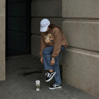Person sitting on steps wearing a brown sweatshirt and blue jeans, with a Starbucks cup nearby.