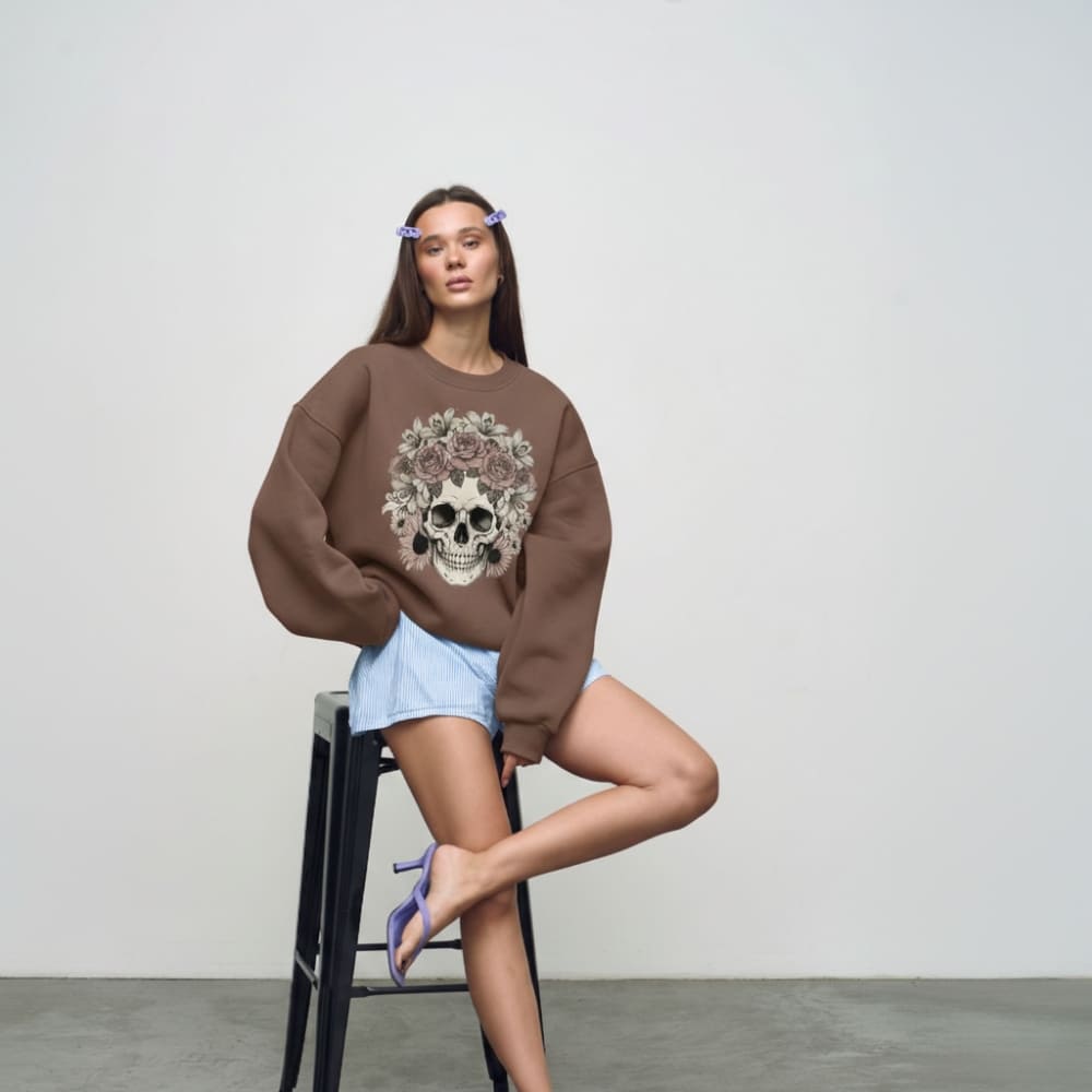 Woman wearing a brown sweatshirt with a skull design, sitting on a black stool against a plain background.