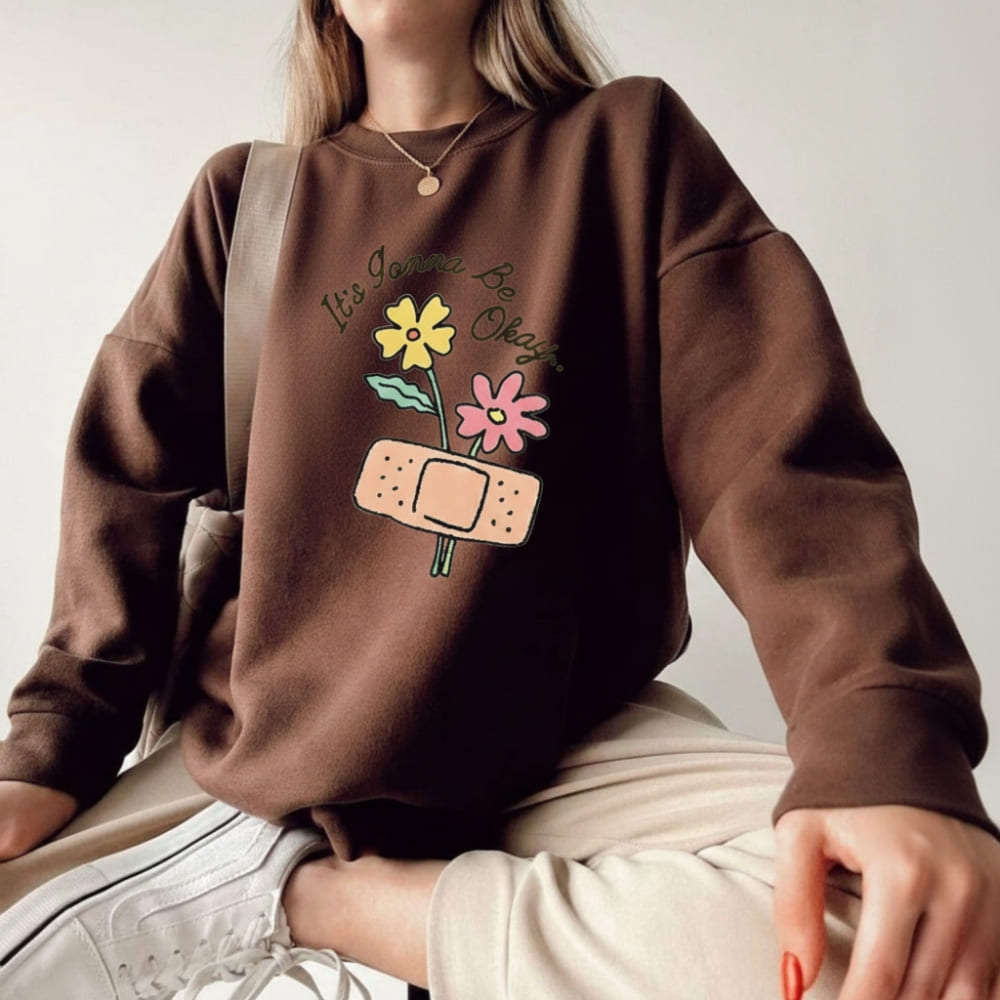 Person wearing a brown sweatshirt with floral and bandage design on a plain background