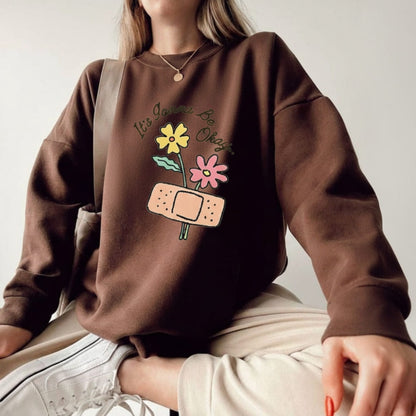 Person wearing a brown sweatshirt with floral and bandage design on a plain background