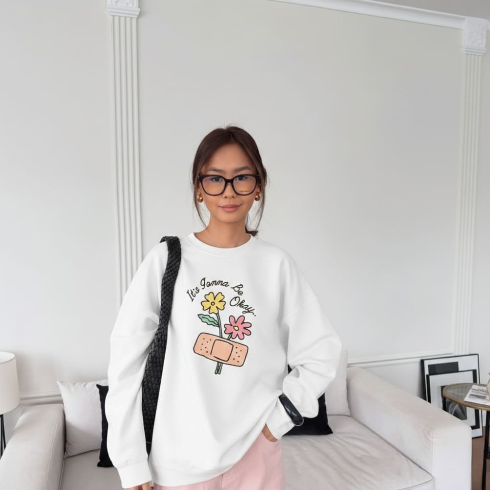 Person wearing a white sweatshirt with colorful graphics and text, standing in a room with a white wall and light-colored furniture.