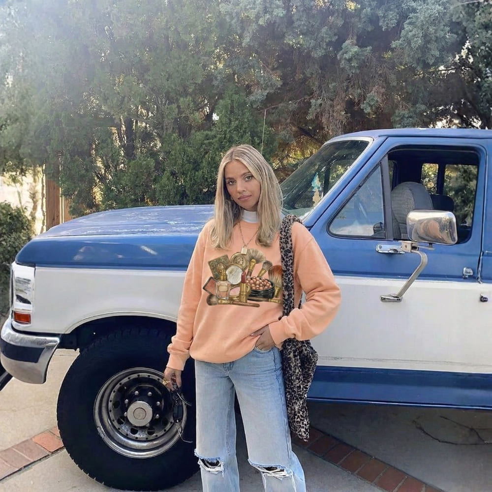 Person wearing a peach sweatshirt with a graphic design, standing in front of a blue and white van.