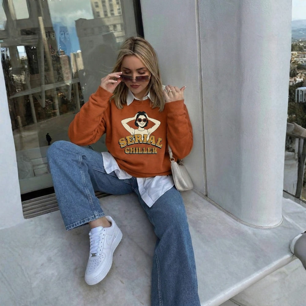 Person wearing an orange sweater with a graphic design, sitting on a rooftop.