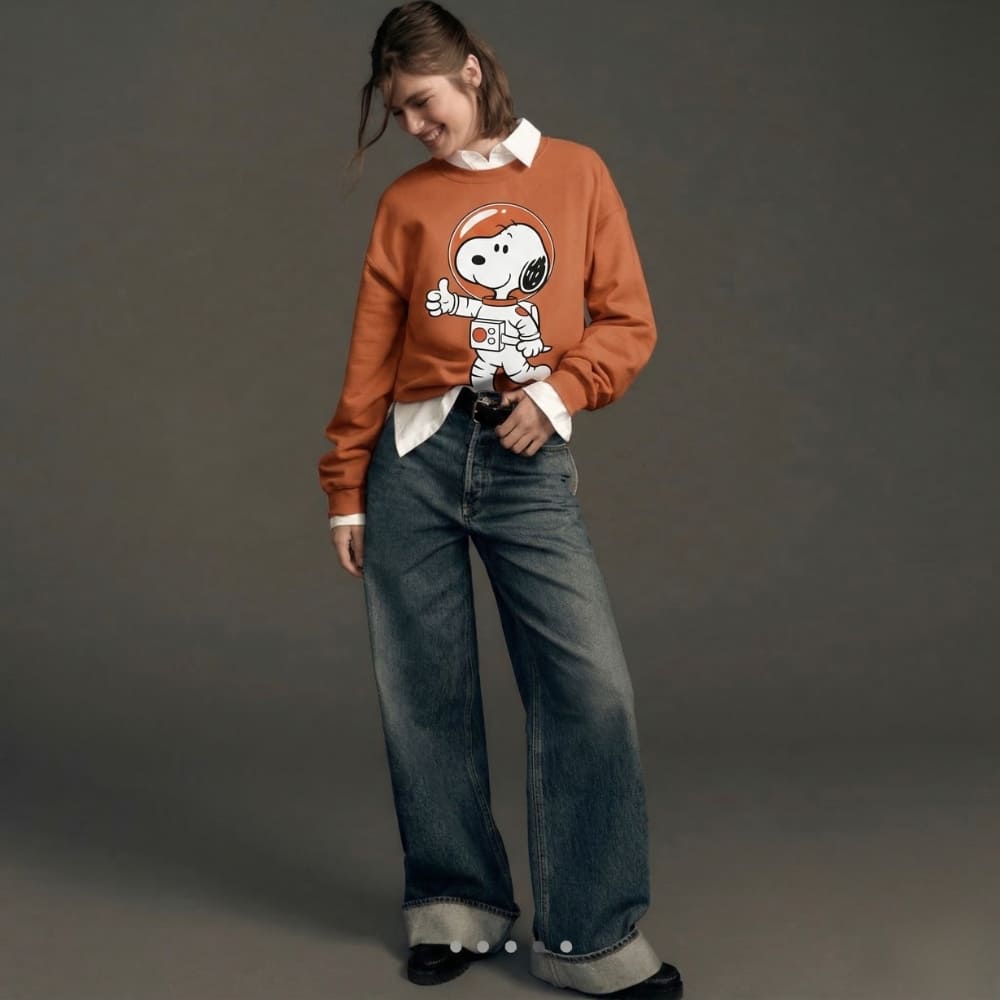 Person wearing a brown sweater with a character design and blue jeans on a gray background
