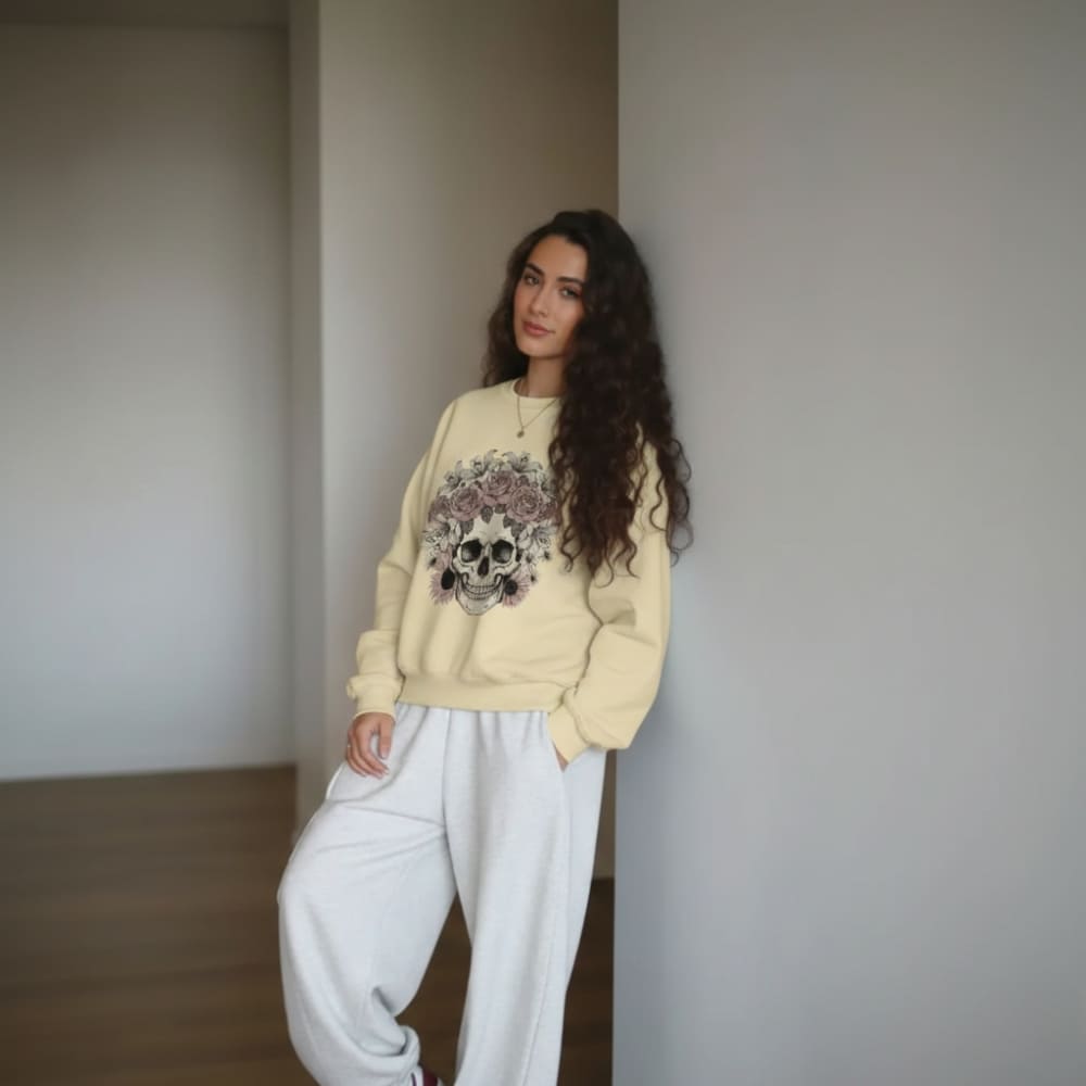 Woman wearing a beige sweater with a floral design and white pants in a minimalistic room.