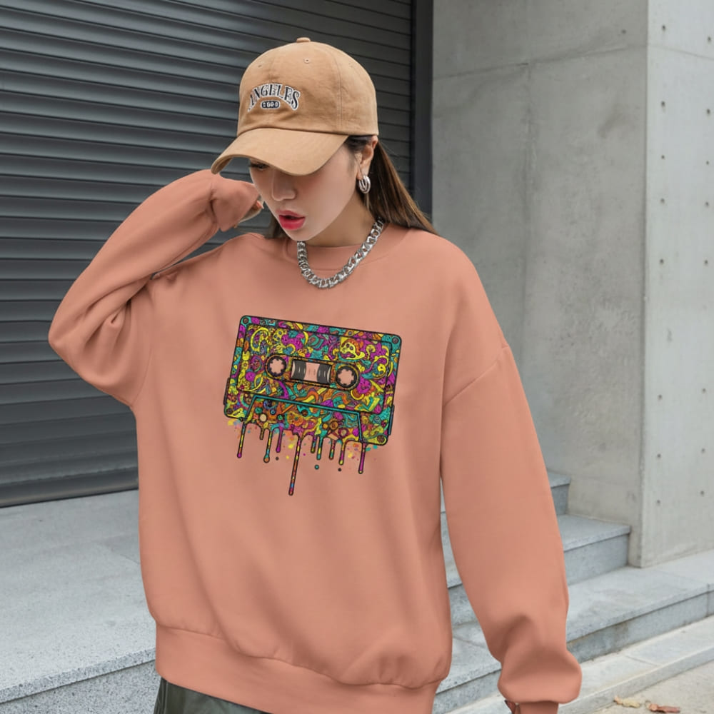 Person wearing a peach-colored sweatshirt with a colorful cassette tape design and a beige cap.