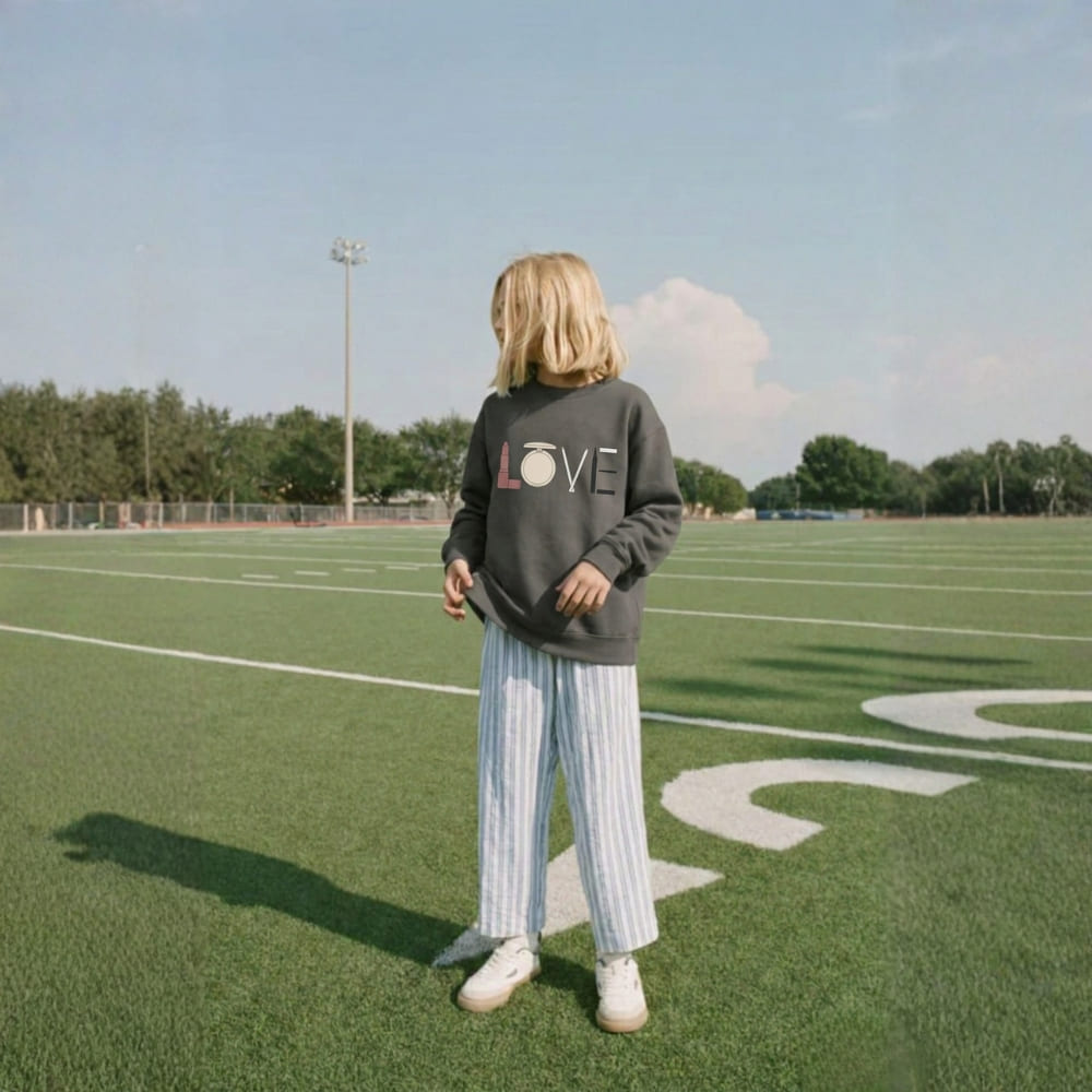 Person standing on a sports field wearing a sweatshirt with 'LOVE' printed on it.