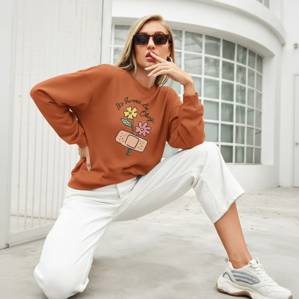 Woman wearing a orange sweatshirt with graphics and text, sitting on a white floor.