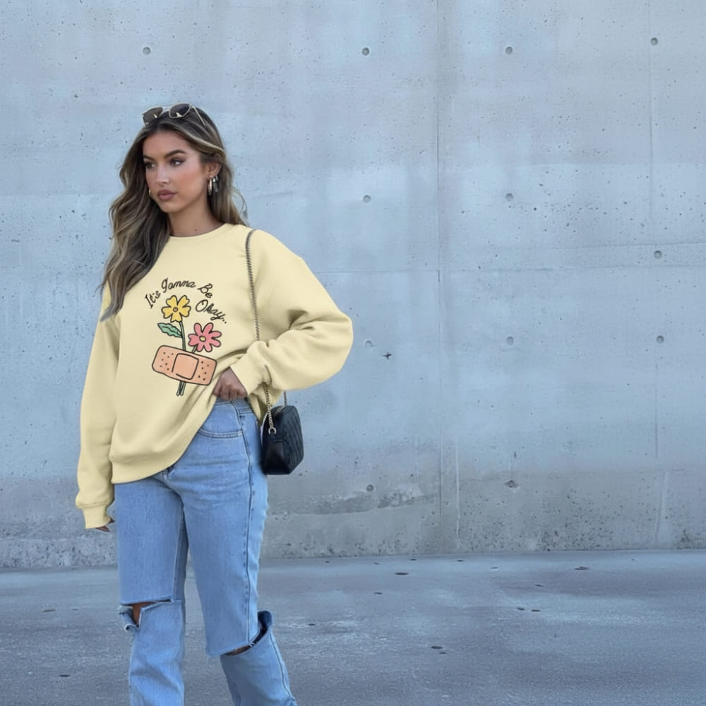 Woman wearing a ivory sweatshirt with floral design against a concrete wall.