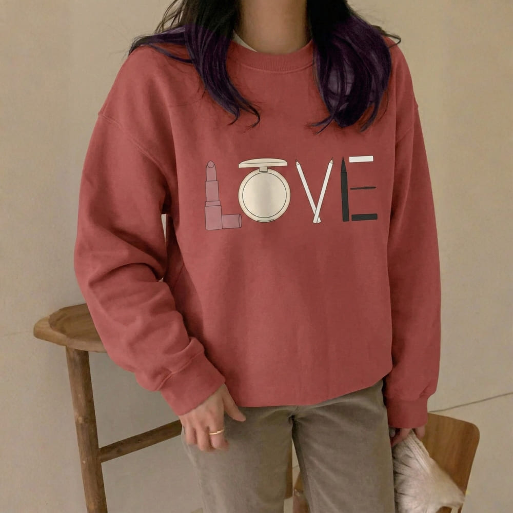 Person wearing a red sweatshirt with 'LOVE' and makeup icons on a beige background