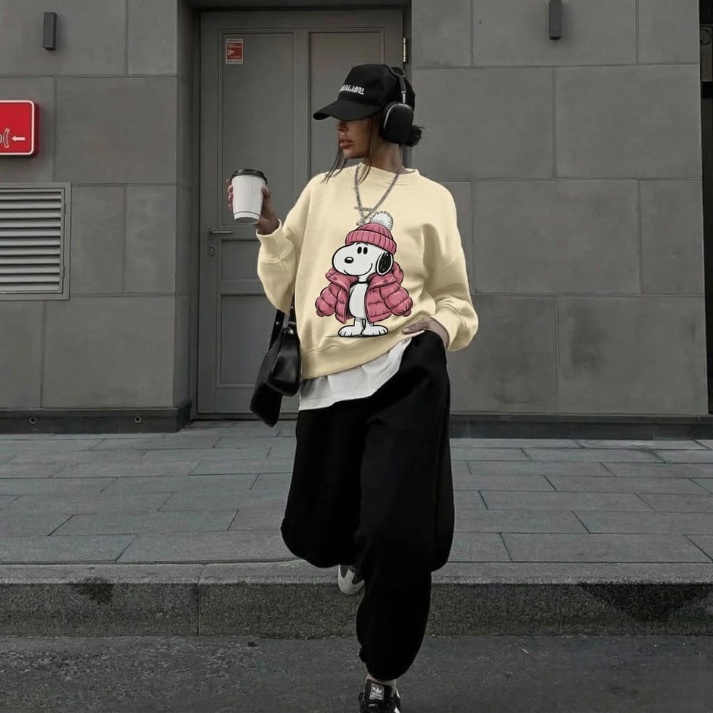Person wearing a beige sweatshirt with a cartoon character, holding a coffee cup, walking on a street.