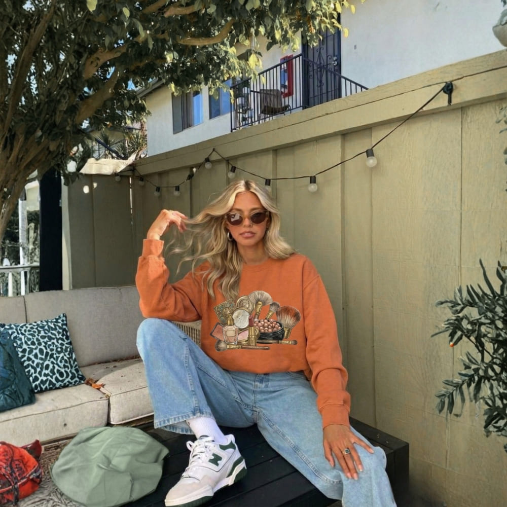 Person wearing an orange sweatshirt with a graphic design, sitting on a bench outdoors.