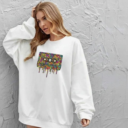 Woman wearing a white sweatshirt with a colorful graphic design against a gray textured wall.
