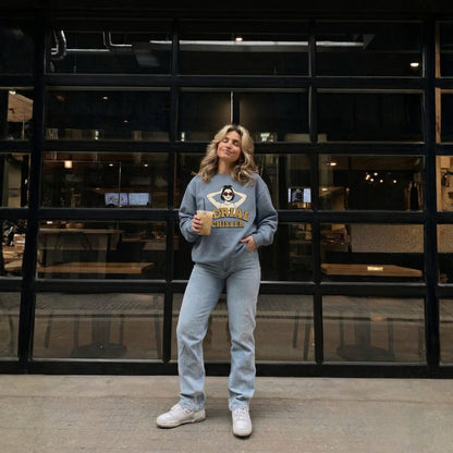 Woman in a blue sweatshirt and jeans standing in front of a glass wall.