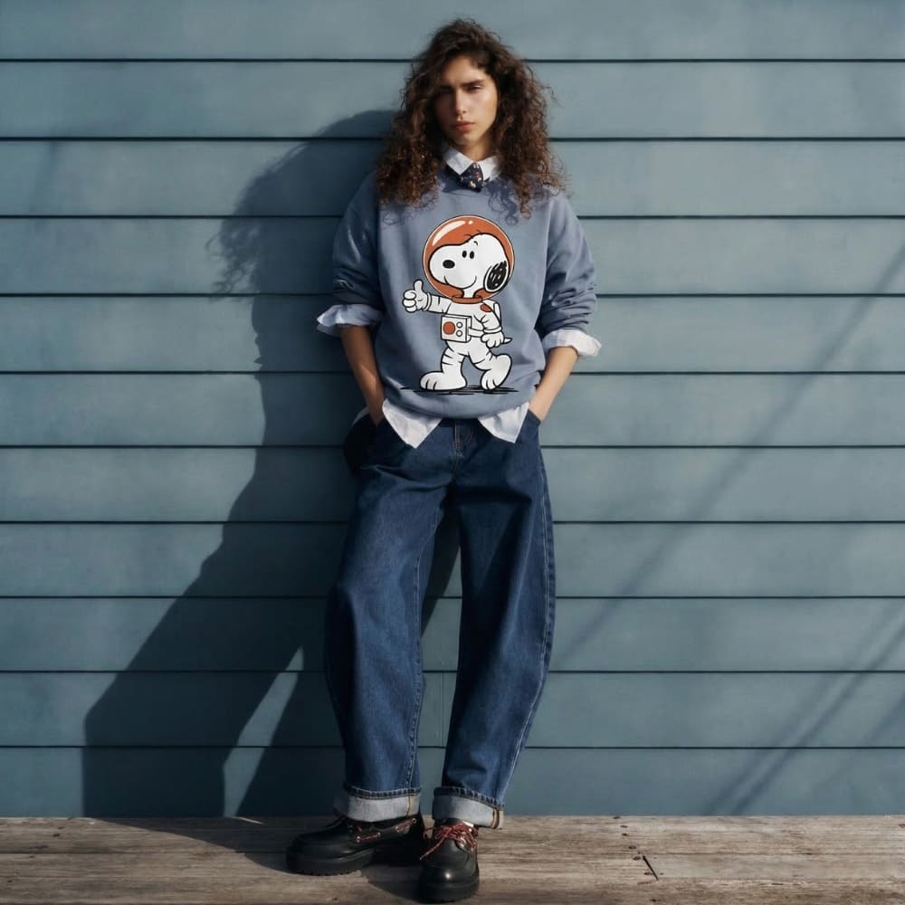 Person wearing a blue sweater with an astronaut graphic against a wooden wall