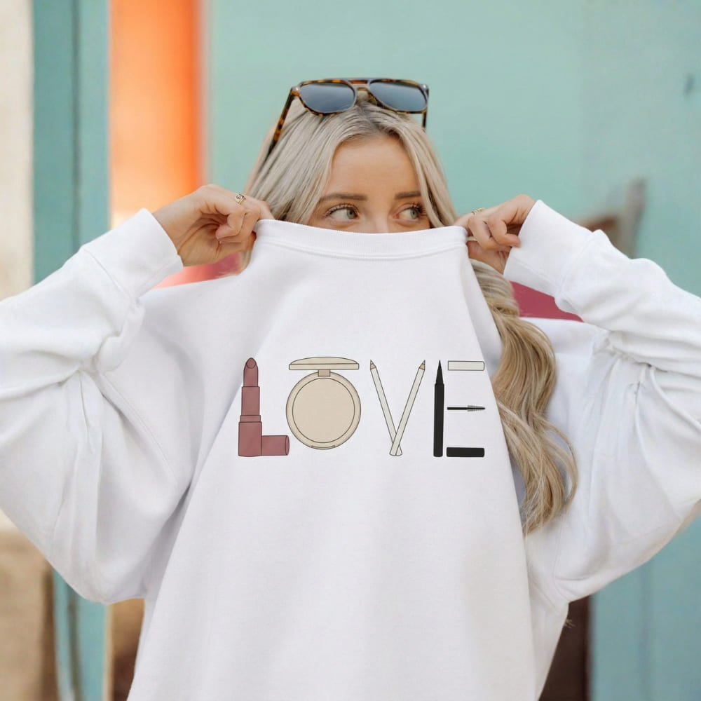 Person holding a white sweatshirt with makeup-themed design