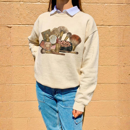 Person wearing a cream sweatshirt with a graphic design of makeup items against a beige wall.
